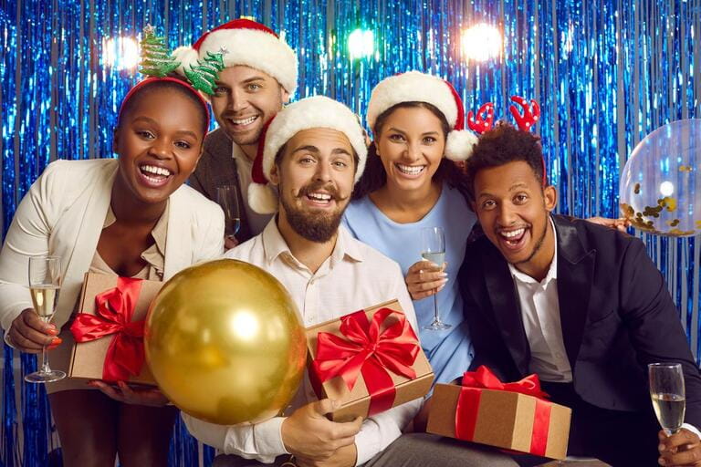 New Year party. Portrait of cheerful young multiracial people having fun together at New Year's party. Friends with glasses of champagne and gift boxes pose against background of shiny foil curtain.