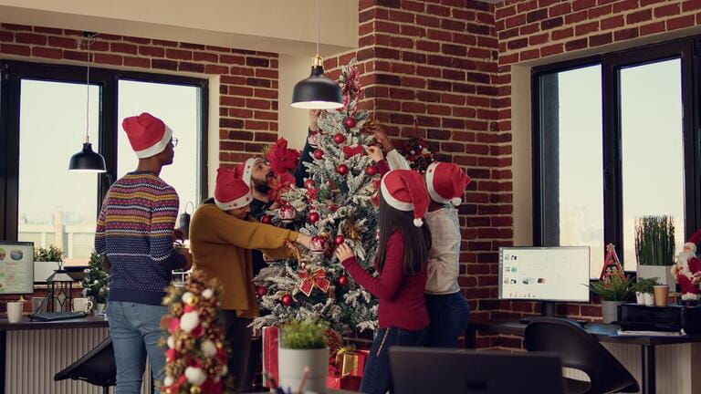 Multiethnic team of people putting christmas tree decor in festive office, preparing for winter season tradition at job. Decorating workplace with xmas ornaments for seasonal holiday. Multiethnic team of people putting christmas tree decor in festive office, preparing for winter season tradition at job. Decorating workplace with xmas ornaments for seasonal holiday.