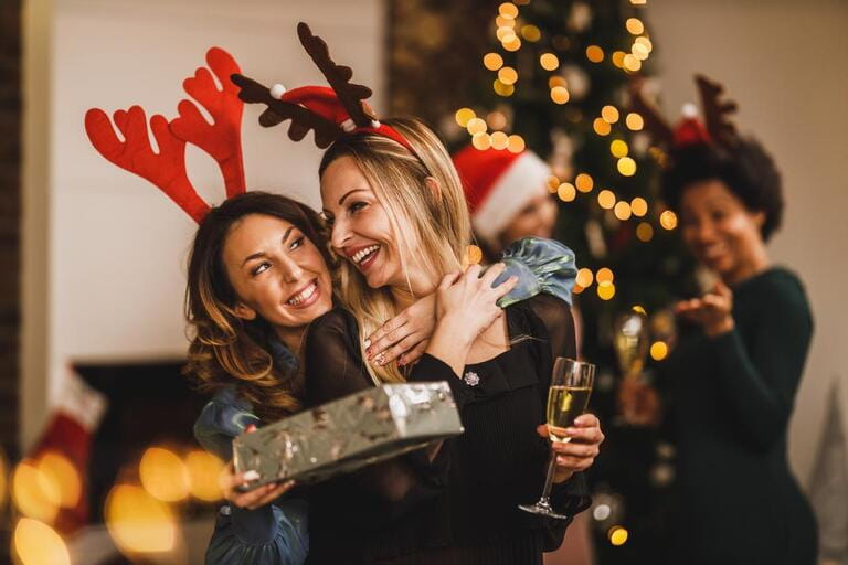 Smiling female friends huging and giving presents to each other while gathering at home to celebrate Christmas or New Year. Smiling female friends huging and giving presents to each other while gathering at home to celebrate Christmas or New Year.