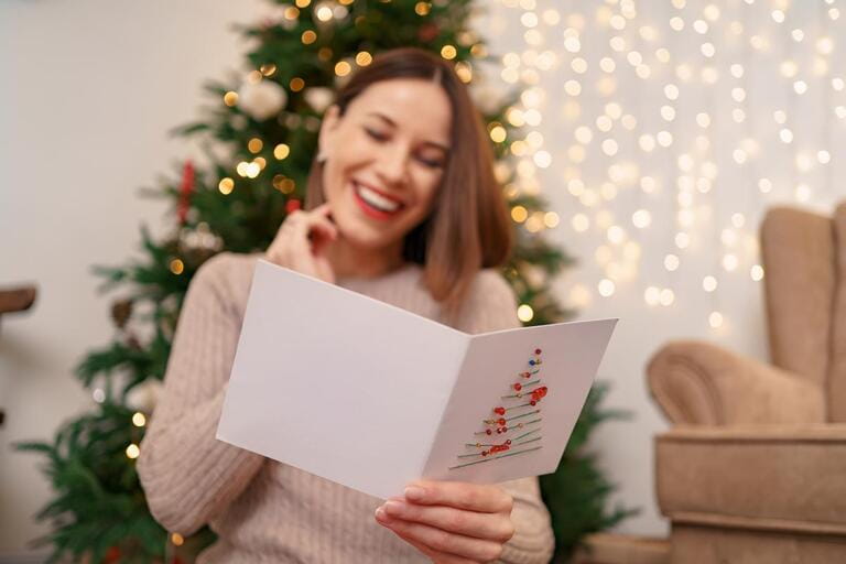 Beautiful woman laughing while reading a Christmas greeting card with light in background. Copy space for text.
