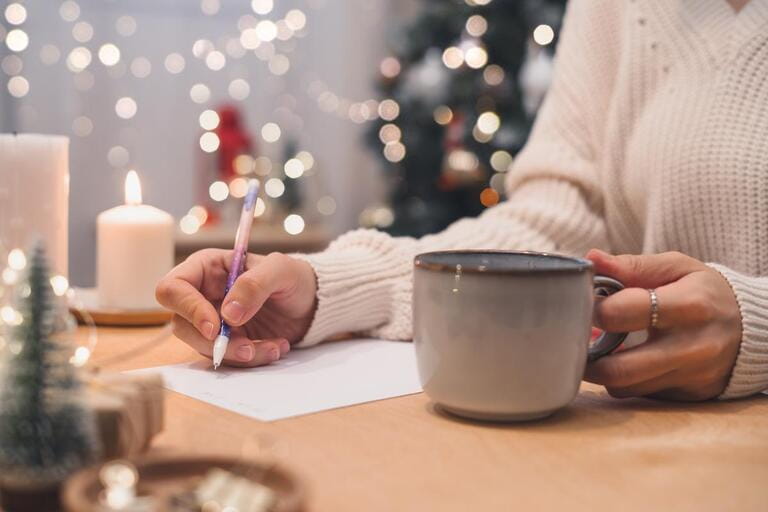 Woman hand holding pen on notepad and coffee cup at home on winter holidays xmas.