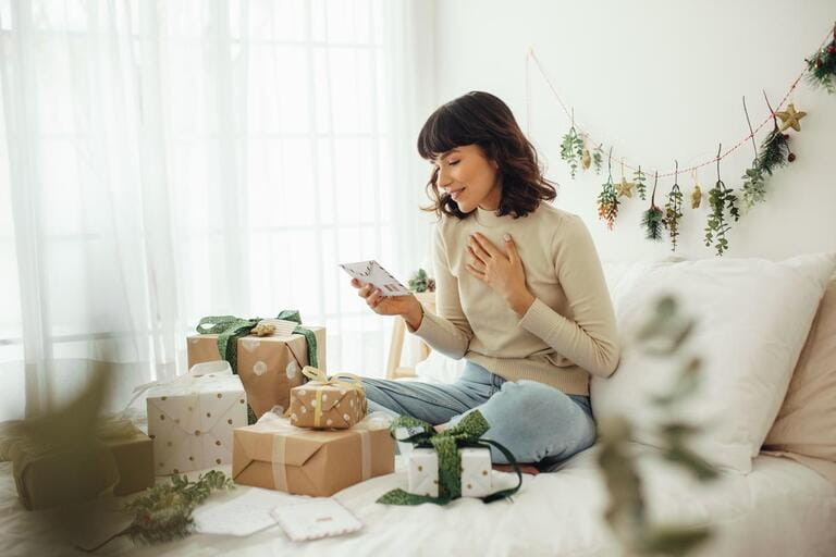 Woman looking at christmas letter. Woman sitting on bed at home with christmas presents and mails.