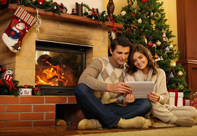 Couple near fireplace in Christmas decorated house with tablet pc Couple near fireplace in Christmas decorated house with tablet pc