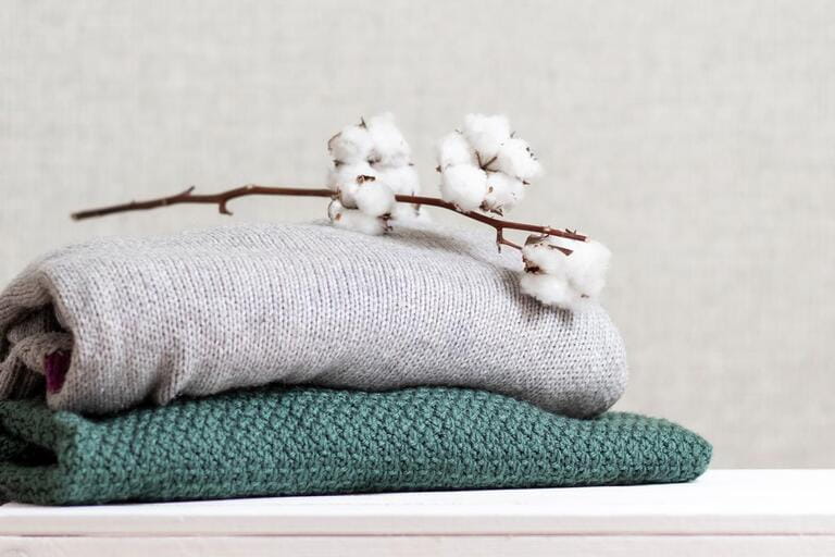 Stack of knitted warm clothes with cotton branch. Stack of knitted warm clothes with cotton branch.