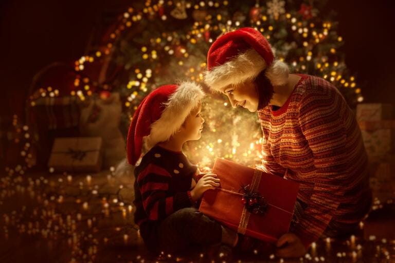 Family opens Christmas illuminated gift boxes in front of the Christmas tree, happy mother with baby in the magical night