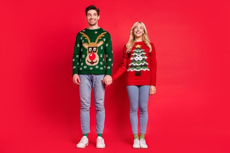 Photo of excited dreamy curious couple hold hands empty space wear ugly sweater jeans shoes isolated red color background Photo of excited dreamy curious couple hold hands empty space wear ugly sweater jeans shoes isolated red color background