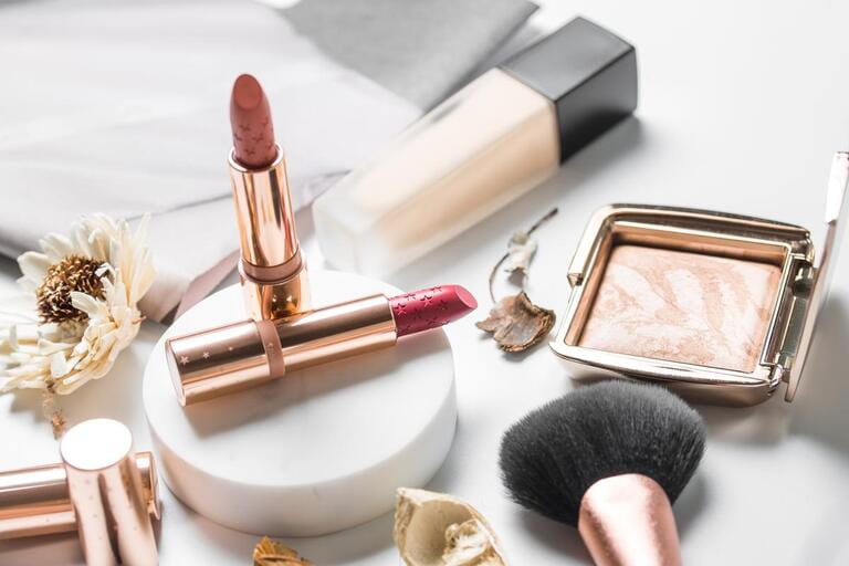 luxury beautiful light design cosmetics makeup brand nude gold orange pink lipstick foundation blusher bronzer brush flower accessories white background