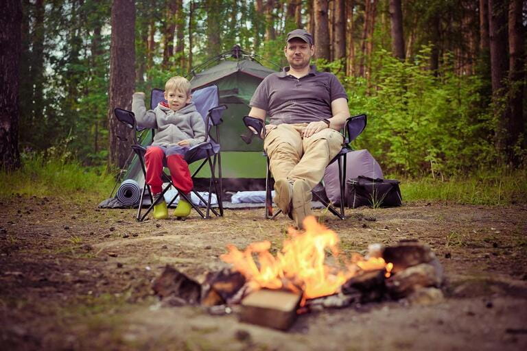 Tourist camp. Man and child sit on chairs in front of a fire near the tents. Tourist camp. Man and child sit on chairs in front of a fire near the tents.