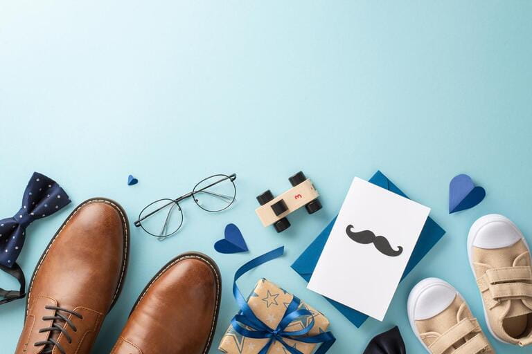 Daddy's little boy shows love on Father's Day with heartfelt gifts. Top view of shoes, tiny sneakers, tie-bow, car toy, glasses, postcard and giftbox on pastel blue background with space for message Daddy's little boy shows love on Father's Day with heartfelt gifts. Top view of shoes, tiny sneakers, tie-bow, car toy, glasses, postcard and giftbox on pastel blue background with space for message