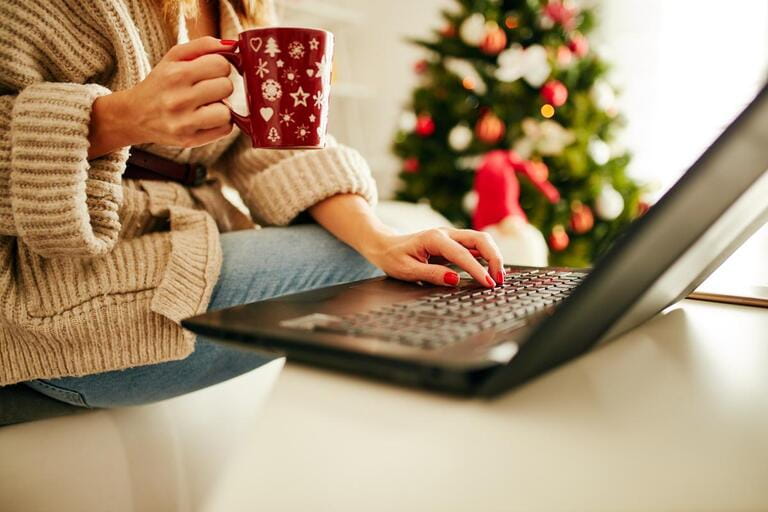 Woman holding cup of coffee while working on laptop at home for Christmas. New Year and Xmas concept. Woman holding cup of coffee while working on laptop at home for Christmas. New Year and Xmas concept.