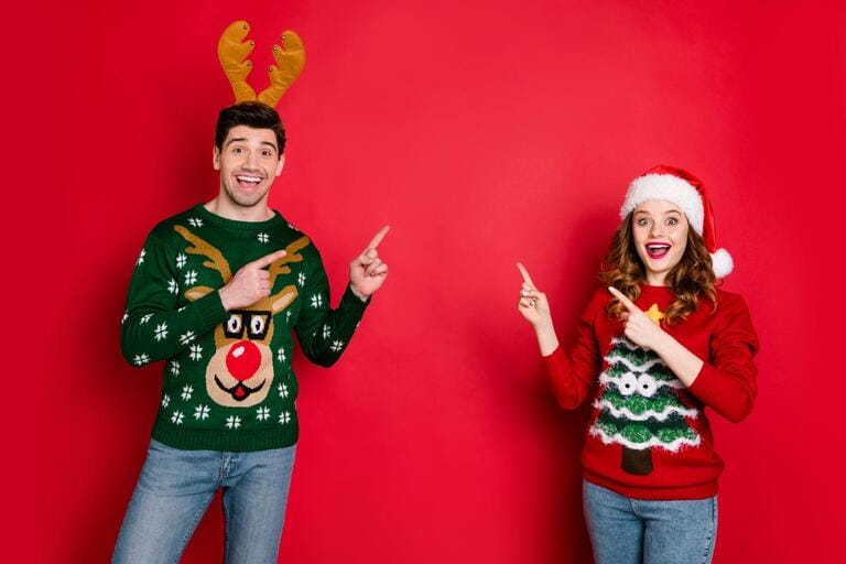 Photo of crazy lady and guy directing fingers empty space on x-mas sale wear funky ugly ornament pullovers isolated red color background Photo of crazy lady and guy directing fingers empty space on x-mas sale wear funky ugly ornament pullovers isolated red color background