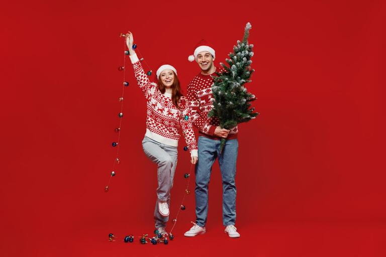 Full body fun happy young couple friends two man woman 20s in sweater hat hold fir-tree garland isolated on plain red background studio Full body fun happy young couple friends two man woman 20s in sweater hat hold fir-tree garland isolated on plain red background studio