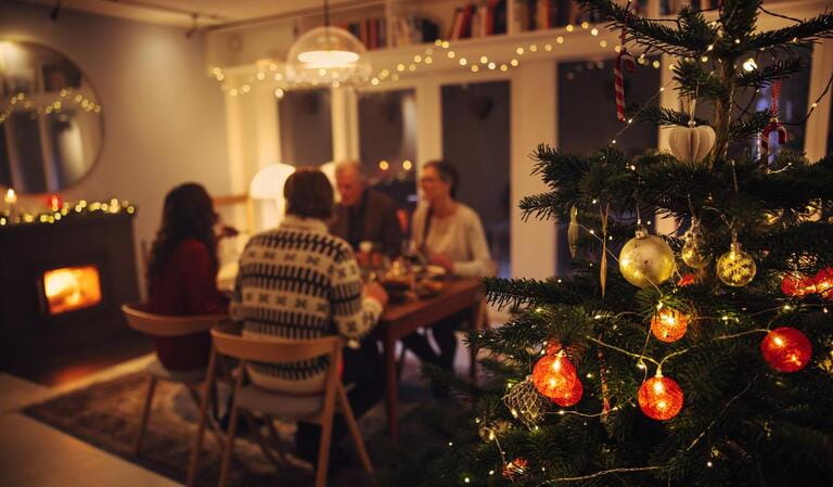 Interior shot of warm cozy Christmas decorated family home. Family sitting at dinner table having a Christmas eve dinner together.