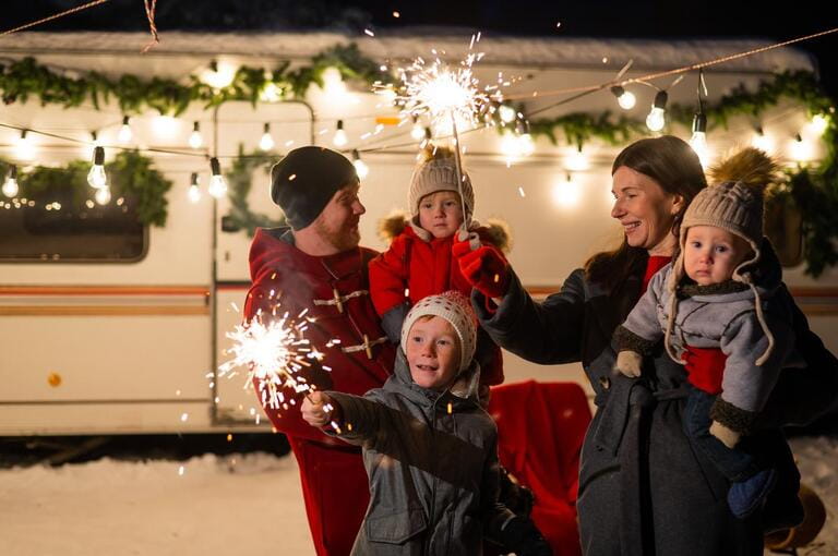 Happy family celebrates christmas in nature and holds sparklers. Parents with three sons travels in a van.