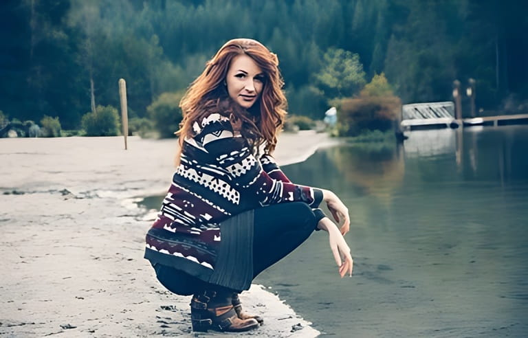 Caucasian Red-Haired Woman Relaxing By The Lake in The Fall. Wearing Fall Fashion. Cowichan-style knitted sweater.