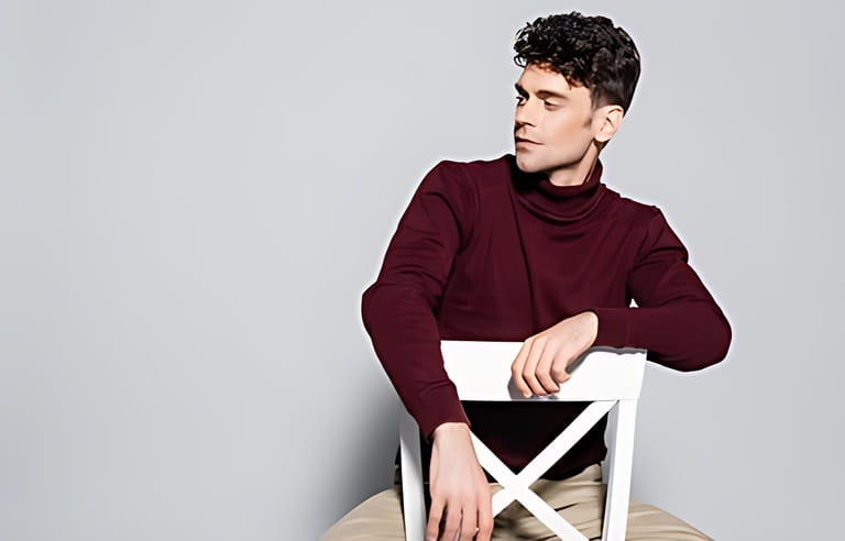 young man in burgundy jumper posing on chair isolated on grey young man in burgundy jumper posing on chair isolated on grey