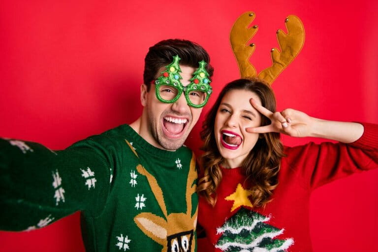 Image of crazy couple making selfie sticking out tongue winking v-sign wearing funny ugly decorations jumpers isolated red background Image of crazy couple making selfie sticking out tongue winking v-sign wearing funny ugly decorations jumpers isolated red background