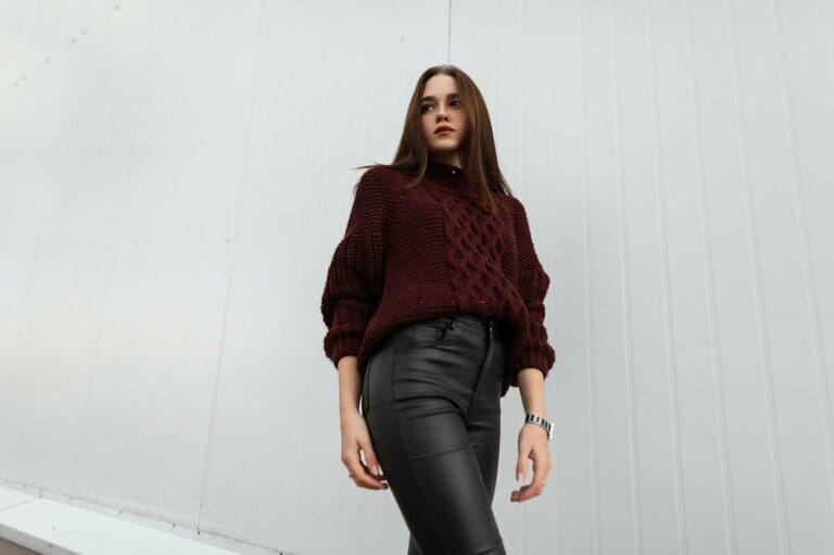 Attractive young woman in a fashionable knitted sweater in stylish black leather pants posing near a modern white wall in the city. Attractive young woman in a fashionable knitted sweater in stylish black leather pants posing near a modern white wall in the city.