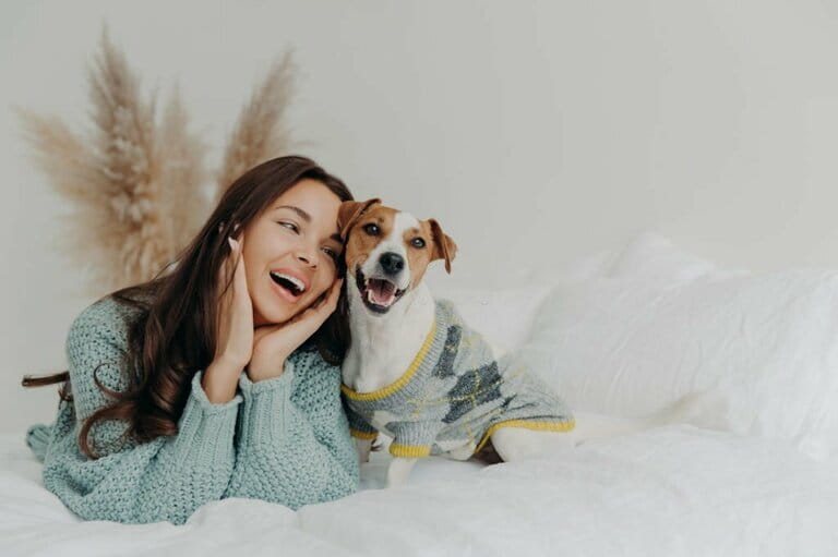 Human and animal concept. Cheerful beautiful young woman showing love to dogs, spending leisure time with pets, lying together in bed, looking tenderly at animals Human and animal concept. Cheerful beautiful young woman showing love to dogs, spending leisure time with pets, lying together in bed, looking tenderly at animals