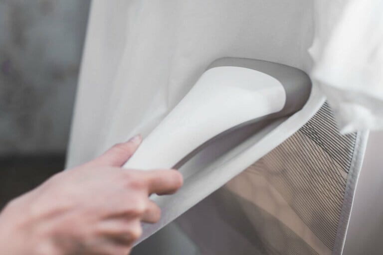 Close-up of steamer in hand steaming white clothes on hanger